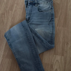 Högmidjade snake jeans (stretchiga) - Säljer ett par ljusblå jeansbyxor i storlek S med klassisk femficksdesign och dragkedja. Jeansen har en något tvättad look och raka ben. Perfekta för dig som gillar en avslappnad och stilren vibe.
