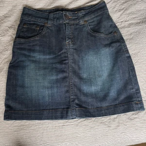 Mörkblå jeanskjol från Lindex - Snygg mörkblå jeanskjol från Lindex storlek 36. Kjolen är i stretchig denim med 98% bomull och 2% elastan. Toppskick. 