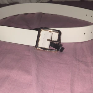 Vitt bälte från BikBok med guldspänne - Stilrent vitt bälte från BikBok i storlek XS-S helt oanvänt. Bältet har ett fyrkantigt guldigt spänne och är gjort i ett slätt material som ger en clean look. Perfekt accessoar för att lyfta din outfit med en enkel men snygg detalj.