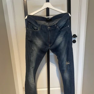 Blå jeans från Pour X, storlek 34/33 - Säljer ett par blå jeans från Pour X i storlek 34/33. Jeansen har en klassisk femficksmodell, lätt slitna detaljer och en snygg tvätt med ljusare partier. De är raka i modellen och har orangea sömmar som kontrast. Perfekta för en avslappnad stil.
