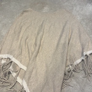 Beige stickad tröja med fransar New Look - Beige stickad tröja utan armar från New Look med snygga fransar längs kanterna. Perfekt för lager-på-lager och chill höst- eller vinterstil. Mjuk och skön känsla, passar dig som gillar avslappnad vibe. OBS! vet tyvärr inte storlek men är lite förstor på mig som är 1,54cm lång.