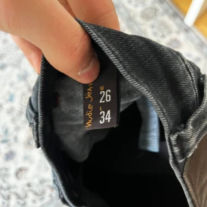 Svarta Nudie Jeans Tight Long John 26/34 - Säljer ett par svarta Nudie Jeans Tight Long John i storlek 26/34. Jeansen är skinny fit med klassisk femficksdesign och har en mörk tvätt. Materialet är 98% bomull och 2% elastan för en stretchig och bekväm känsla.