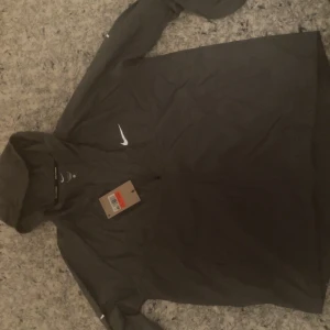 Nike running vindjacka - Säljer en grå vindjacka från Nike Running med huva och dragkedja. Jackan har en stilren design med Nike-logga på bröstet och är tillverkad i lätt polyester. Perfekt för löpturen eller när du vill ha en sportig look. Passar mellan S-M