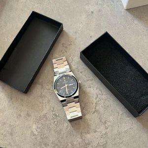 Silverfärgad klocka från Poedagar - Stilren klocka från Poedagar med silverfärgat metallarmband och mörk blå urtavla. Klockan har dag- och datumvisning samt klassisk kvartsrörelse. Levereras i originalask och extra länk medföljer. Perfekt för dig som gillar snygga accessoarer.