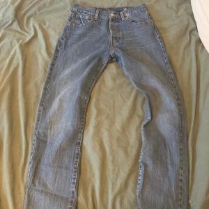 Levi's 501 blå jeans W29 L32 - Klassiska Levi's 501 jeans i ljusblå denim med raka ben och femficksmodell. Byxorna har normal midja, knappgylf och den ikoniska läderpatchen bak. Perfekta för dig som gillar tidlös stil och vill ha ett par riktigt schyssta jeans.