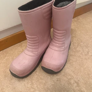 Rosa fodrade stövlar med platt sula - Säljer ett par rosa stövlar med platt sula och rund tå. Insidan är fodrad med grått ullmaterial som håller fötterna varma. Yttermaterialet är syntet och har quiltade detaljer framtill. Perfekt för kalla dagar och enkel att dra på.