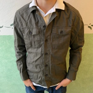 Olivgrön skjorta från Riley slim fit - Snygg olivgrön skjorta från Riley i slim fit-modell. Skjortan har två bröstfickor med knappar, klassisk krage och långa ärmar. Perfekt för dig som gillar en stilren look med lite militärvibbar. Tillverkad i bomull för skön känsla.