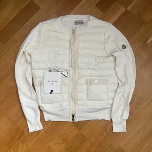Vit cardigan jacka från Moncler - Snygg vit cardigan jacka från Moncler med quiltad front, två fickor och dragkedja. Ärmarna är stickade och har Moncler-logga på vänster arm. Perfekt för lager-på-lager och stilren look. Priset kan diskuteras 