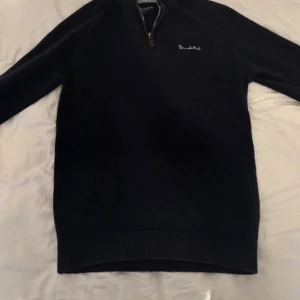 Mörkblå half zip tröja Bondelid - Mörkblå stickad tröja från Bondelid med halv dragkedja och broderad logga på bröstet. Tröjan har ribbade muddar och en ljusgrå insida vid kragen. Perfekt för lager-på-lager och chill stil.