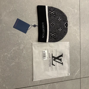 Svart och vit mössa  - Exklusiv svart och vit mössa från H&M med klassiskt monogram och logotyp. Mössan har en bred svart kant med vit rand och är stickad i mjukt material. Perfekt accessoar för dig som vill ha en lyxig och stilren look.