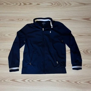 Mörkblå vindjacka Polo Ralph Lauren XL - Snygg mörkblå vindjacka från Polo Ralph Lauren i storlek (18/20) vilket motsvarar storlek s.                              Perfekt för blåsiga dagar