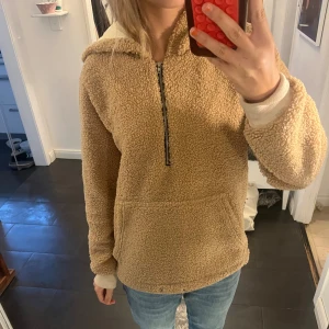 Beige teddy hoodie med huva och half zip - Supermysig beige teddy hoodie med huva och halv dragkedja framtill. Tröjan har en stor magficka och ribbade muddar vid ärmsluten. Perfekt för kyliga dagar och chill outfits.🤎