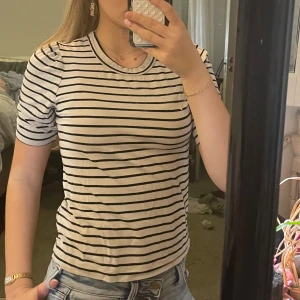Randig t-shirt från Lindex XS - Säljer en klassisk vit t-shirt med svarta horisontella ränder från Lindex i storlek XS. T-shirten har rund halsringning och korta ärmar. Perfekt till jeans eller kjol för en enkel och stilren look.