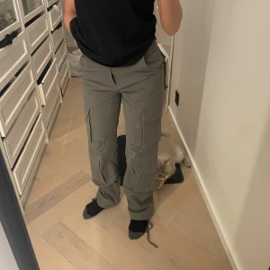Grå cargopants från Luxe To Kill - Säljer ett par grå cargopants från Luxe To Kill med flera stora fickor på benen och baktill. Byxorna har raka ben med dragsko nertill. Perfekta för en avslappnad och trendig streetstyle.