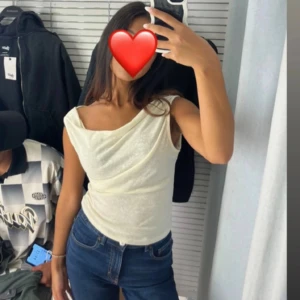 Krämvit top - Säljer min snygga top med tyg som hänger framtill, det går att bära tröjan på några olika sätt. Den är i ett mjukt material och väldigt stretchig.