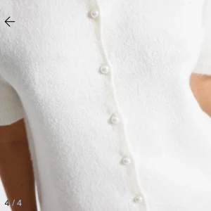 Vit stickad blus med pärlknappar - Superfin vit stickad blus med korta ärmar och rund halsringning. Framsidan har dekorativa pärlknappar som ger en söt och stilren look. Använd ca 2 gånger, därav nytt skick. Orginalpris 125kr🌸