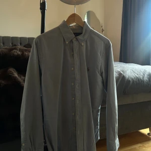 Grå skjorta från Ralph Lauren - Klassisk grå skjorta från Ralph Lauren i slim fit-modell. Skjortan har knappar hela vägen, button down-krage och den ikoniska broderade loggan på bröstet. Tillverkad i mjuk bomull och har långa ärmar. Perfekt för en clean och stilren look.