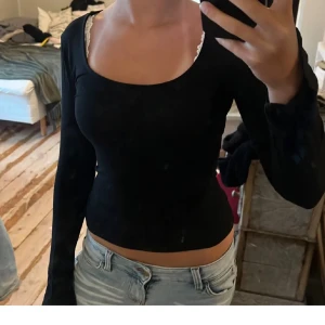 Svart långärmad topp med rund hals - Säljer en svart långärmad topp med rundad halsringning och slim passform. Toppen är croppad och har en enkel, stilren design som passar perfekt till jeans eller kjol. Materialet känns mjukt och stretchigt mot huden.