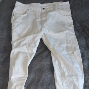 Vita jeansbyxor med slitningar - Snygga vita jeansbyxor med klassisk femficksdesign och diskreta slitningar på benen. Byxorna har raka ben och normal passform, perfekta för en fräsch och stilren look. Tillverkade i bomull för skön känsla hela dagen.