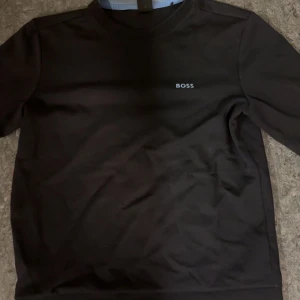 Svart långärmad tröja från BOSS - Säljer en stilren svart långärmad tröja från BOSS med diskret logga på bröstet. Tröjan har en klassisk passform och är tillverkad i mjuk bomull som känns skön mot huden. Perfekt för dig som gillar en clean och enkel look.