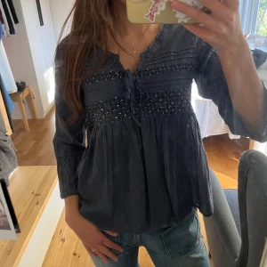 Mörkblå blus med broderi och pärlor - Supersöt mörkblå blus från Odd Molly med broderade detaljer och små pärlor framtill. Blusen har knytband vid halsen, v-ringad öppning och trekvartsärmar. Den är i storlek 38 men jag är storlek 34 så skulle säga att den passar 34-38