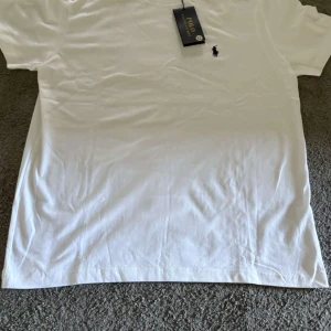 Vit t-shirt från Polo Ralph Lauren - Snygg vit t-shirt från Polo Ralph Lauren med klassisk logga broderad på bröstet. T-shirten har rund hals och korta ärmar, tillverkad i mjuk bomull som känns skön mot huden. Perfekt för en clean och stilren look.