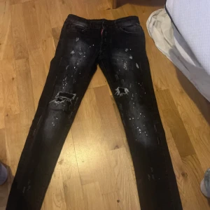 Svarta  jeans från Dsquared2 - Snygga svarta jeans från Dsquared2 med skinny passform och coola slitningar samt vita färgstänk. Byxorna har dragkedjor på bakfickorna och klassisk femficksdesign. Materialet är jeans och de har en modern, streetinspirerad look. Dem är långa i benen 
