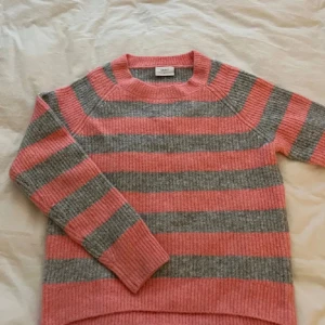 Färgglad randig tröja - Supermysig stickad tröja från Grunt i breda rosa och grå ränder. Tröjan har rund halsringning, ribbade muddar och lång ärm. Perfekt för dig som gillar en chill och färgglad stil under kyliga dagar. L motsvarar S