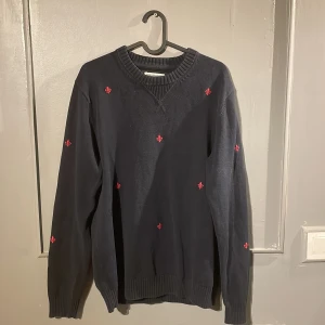 Mörkblå stickad tröja Morris Gents  - Snygg mörkblå stickad tröja från Morris Gents i storlek medium. Tröjan har broderade röda detaljer över hela plagget och ribbade muddar vid hals, ärmslut och nederkant. 