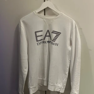 Vit EA7 Emporio Armani sweatshirt - Snygg vit sweatshirt från EA7 Emporio Armani med stor logga framtill. Tröjan har rund halsringning och långa ärmar. Finns några märken på tröjan vid armen finns bild