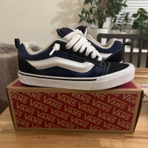 Vans Knu Skool blå/vita sneakers - Säljer ett par Vans Knu Skool sneakers i marinblått och vitt med klassisk vit sula och tjocka vita skosnören. Skorna har den ikoniska sidovågen och är tillverkade i mocka och textil. Perfekta för dig som gillar streetstyle och skatekänsla. Kommer med box och digitalt kvitto 