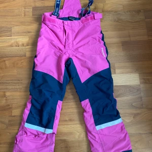 Rosa och marinblå täckbyxor Didriksons!! - Täckbyxor från Didriksons i rosa och marinblått med hängslen och reflexdetaljer. Byxorna har hög midja och förstärkta knän, perfekta för vinterns alla äventyr. Justerbar midja och slitstarkt material som står emot väder och vind.