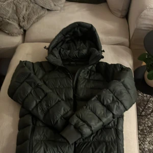 Grön pufferjacka Peak Performance 170 - Säljer en görn pufferjacka från Peak Performance i storlek 170. Jackan har huva, dragkedja och ribbade muddar vid ärmsluten. Perfekt för kalla dagar och riktigt skön att ha på sig. Broderad logga på bröstet. Knappt använd, Ny skick. Hör av er om ni har några frågor. Pris kan diskuteras!