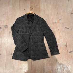 Rutig kavaj från Oscar Jacobson - Snygg grå kavaj från Oscar Jacobson med rutig design i vitt. Klassisk passform med smala slag, helfodrad insida och knappar vid ärmslut. Perfekt för dig som vill ha en stilren och tidlös look. Materialet känns mjukt och exklusivt.