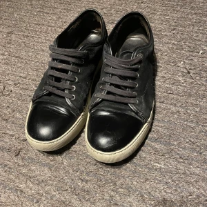 Svarta sneakers från Lanvin - Snygga svarta sneakers från Lanvin med klassisk vit sula och svart tå i skinn. Ovandelen är i mocka och skorna har svarta snören. Perfekta för dig som gillar stilrena och exklusiva sneakers med en lyxig känsla. Pris kan förhandlas vid snabb affär:)