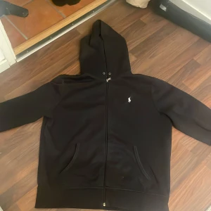 Svart hoodie från Polo Ralph Lauren - Svart hoodie från Polo Ralph Lauren med dragkedja och klassisk logga på bröstet. Tröjan har  luva, fickor framtill och är tillverkad i mjuk bomullsblandning. Perfekt för chill dagar eller när du vill ha en clean streetstyle-look!! kan sänka pris ned 100kr- 