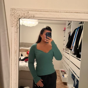 Grön ribbad stickad tröja med v-ringning - Snygg grön stickad tröja med ribbad struktur och djup v-ringning. Tröjan har lång ärm och sitter figurnära med en feminin passform. Perfekt för dig som gillar en enkel men trendig look.