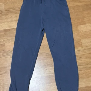 Mörkblå mjukisbyxor från Kappahl - Mörkblå mjukisbyxor från Kappahl med dragsko i midjan och resår vid bensluten. Byxorna är tillverkade i mjukt material och har en avslappnad passform, perfekta för chill dagar eller när du vill vara bekväm. Dom är använda men väldigt bra skick 