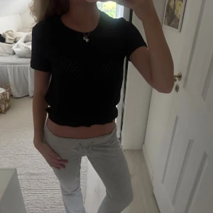 Svart croppad topp med hålmönster - Säljer en svart croppad topp med korta ärmar och rund hals. Toppen har ett snyggt hålmönster och elastisk kant nedtill som ger en cool volang-effekt. Perfekt för dig som gillar en enkel men trendig look.