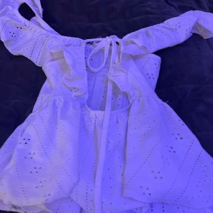 Vit kort klänning med snörning - Supersöt vit blus med broderade detaljer och offshoulder-ärmar. Blus har snörning i ryggen och volang vid axlarna. Perfekt för alla tillfällen, med ett luftigt och romantiskt uttryck.🤍