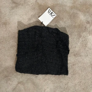 Svart glittrig tubtopp från Zara - Svart tubtopp/korsett från Zara i storlek XS. Toppen har ett glittrigt tyg med struktur och dragkedja på sidan. Prislapp kvar, nypris 559kr