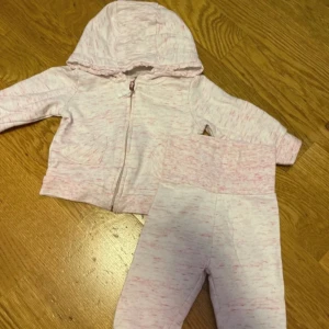 hoodie med dragkedja occ byxor- 3-6 mån 62 cm  - Söt ljusrosa hoodie med dragkedja och huva, dekorerad med små hjärtformade fickor. Tröjan har långa ärmar och är tillverkad i mjuk bomullsmix. Perfekt för mysiga dagar och enkel att matcha med andra plagg.