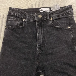 Svarta jeans från Zara, storlek 36 - Snygga svarta jeans från Zara i storlek 36. Jeansen har klassisk femficksdesign, hög midja och raka ben. Det ända som är sönder är vid sidan där bak där den man lägger skärp i har gått isönder.