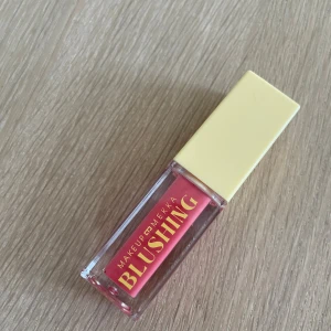 Makeup Mekka Blushing flytande rouge - Flytande rouge från Makeup Mekka i en snygg rosa nyans. Kommer i en genomskinlig fyrkantig tub med gul kork och text i guld. Perfekt för att ge kinderna en fräsch och naturlig färg.