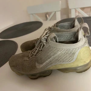 Nike Vapormax Flyknit beige sneakers - Säljer ett par Nike Vapormax Flyknit sneakers i beige med stickad ovandel och transparent sula. Skorna har snörning och en sportig, storlek 40. Lite skitiga men det går troligen att fixa! .