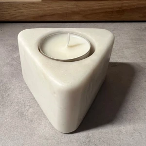 Triangulär ljushållare i vit marmor - Elegant triangulär ljushållare i vit marmor, perfekt för värmeljus. Ger en modern och stilren känsla till hemmet. Inga synliga skador eller slitage, ser ut att vara i mycket gott skick. Passar utmärkt som dekoration eller present.