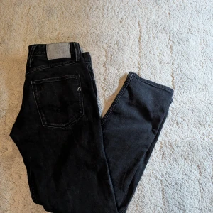 Svarta Replay jeans, storlek 31 - Snygga svarta jeans från Replay med klassisk femficksdesign och diskret Replay-logga på fickan. Jeansen har en rak passform och är tillverkade i mjukt jeanstyg med silverfärgade detaljer. Perfekt för dig som gillar stilrena och tidlösa jeans.
