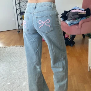 Ljusblå jeans med rosa rosetter - Säljer ett par ljusblå jeans med raka ben. På bakfickorna finns broderade rosa rosetter som ger en söt och unik touch. Jeansen är i klassisk denim och har en avslappnad passform, perfekta för dig som gillar detaljer. Från edikted i storlek XS, mycket bra skick. 