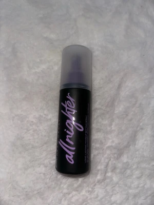 Urban Decay All Nighter Face Mist - Urban Decay All Nighter face mist i svart flaska med lila text. Sprayen har en matt finish och kommer med en praktisk spraypump och genomskinligt lock. Perfekt för att fixera sminket och hålla det på plats hela dagen.