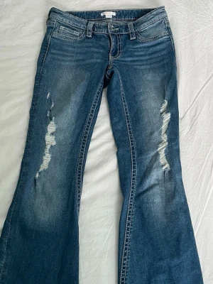 Lågmidjade jeans med slitningar - Säljer ett par blå bootcut jeans med snygga slitningar på framsidan och coola detaljer på bakfickan. I princip oanvända. Passar mig som är ca 168 cm.